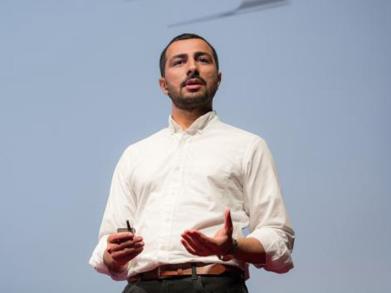 Image of Dr. Muneeb Ali wearing a white shirt in front of a large blue screen